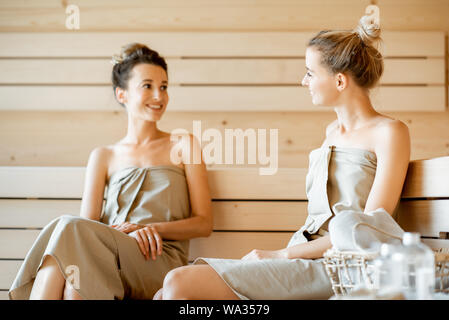 Due giovani fidanzate avente allegro conversazione durante i momenti di relax nella sauna. Concetto di amicizia femminile e il trattamento termale Foto Stock