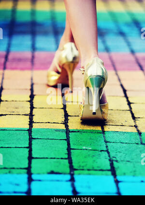 Bella giovane donna in golden stilettos camminando sulla colorata lgbt zebra crossing Foto Stock