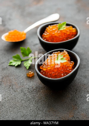 Caviale rosso in recipienti su un vecchio sfondo nero Foto Stock