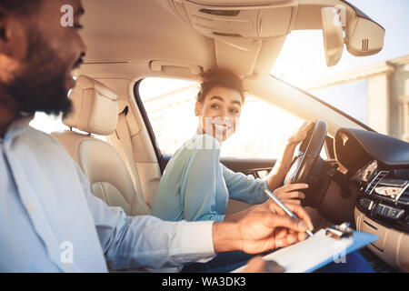 Donna felice in esame auto, sorridente di istruttore maschio Foto Stock