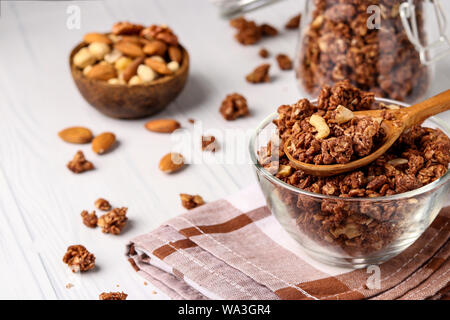 Il Granola muesli croccanti con miele naturale, il cioccolato e i dadi in una ciotola di vetro contro uno sfondo bianco, cibo sano, close-up, orientatio orizzontale Foto Stock