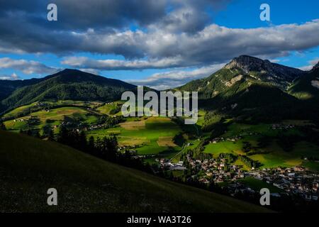 Bellissimo scatto di verdi colline ed edifici vicino a campi erbosi con alberi sotto un cielo blu Foto Stock