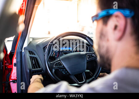 Il tecnico con gli occhiali di sicurezza avviamento del motore di un auto rossa nel corso di una ispezione del veicolo Foto Stock