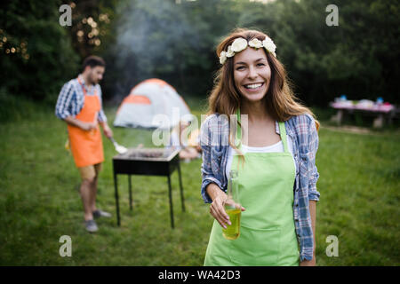 Gruppo di persone felici intorno permanente grill, chat, bere e mangiare. Foto Stock