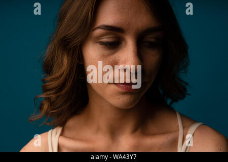 Sottolineato giovane donna confusa circa le rughe del viso invecchiamento della pelle sulla fronte o corvi piedi guardando la telecamera isolata su sfondo per studio, sconvolto worrie Foto Stock