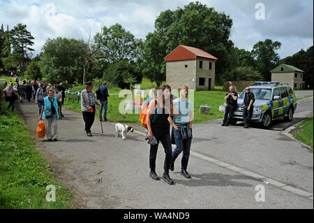Warminster, Wiltshire, Regno Unito. Il 17 agosto 2019. I visitatori di Imber chiesa passano da MOD a guardia di polizia Ministero della Difesa urban assault case di formazione. Oltre 30 gli autobus londinesi, prevalentemente Routemasters classic, raccogliere in Warminster per eseguire un servizio di autobus per il "villaggio perduto" di Imber su Salisbury Plain. Il villaggio fu requisita per la seconda guerra mondiale ai fini della formazione nel 1943 ed è rimasta una parte di MOD basi di formazione da sempre, tranne che per un open day per anno. G.P.Essex/Alamy Live News Foto Stock