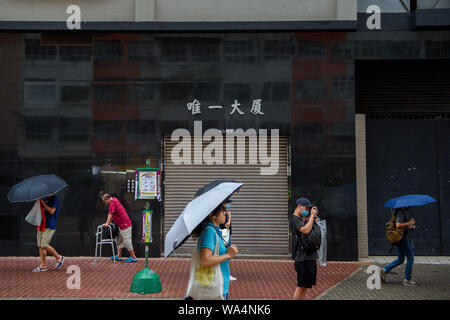 Hong Kong Cina. 17 Ago, 2019. Un uomo, piegata con un aiuto a piedi, passeggiate lungo un sentiero nel distretto di Kowloon, passando un ingresso garage e altri passanti. Credito: Gregor Fischer/dpa/Alamy Live News Foto Stock