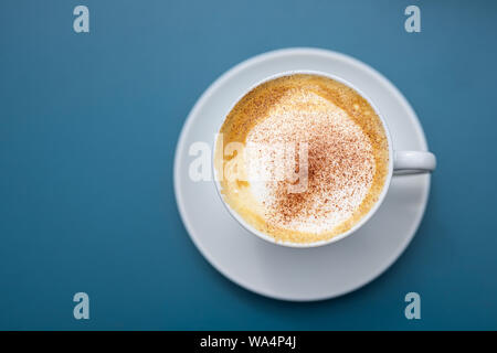 Tazza di cappuccino con cacao in polvere su uno sfondo blu, vista direttamente dal di sopra, spazio copia selezionata, focus, molto stretta la profondità di campo Foto Stock