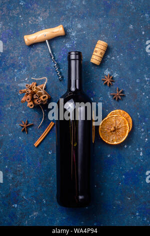 Bottiglia di vino rosso con un cavatappi e gli ingredienti per la produzione di vino brulé su uno sfondo blu scuro. Inverno bere concept Foto Stock