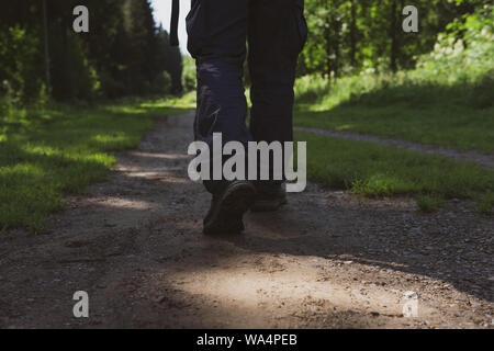 Un uomo cammina lungo un ombroso sentiero forestale, solo le gambe sono visibili da dietro Foto Stock