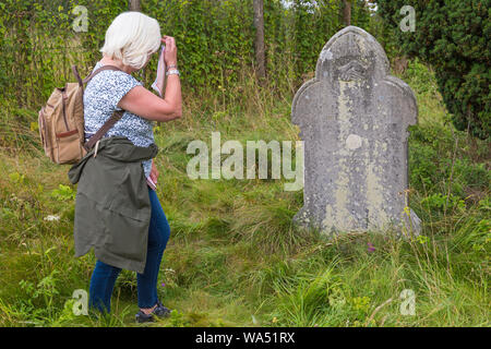 Imber, Wiltshire, Regno Unito. 17 ago 2019. Trasportati indietro ai giorni passati! Migliaia di visitatori a sfruttare al massimo le opportunità di scoprire il perso il villaggio di Imber ed esplorare Imber Chiesa su Salisbury Plain su uno speciale Open Day, evento Imberbus. La popolazione civile di Imber village è stato sfrattato nel 1943 durante la Seconda Guerra Mondiale e rimane un villaggio disabitato, utilizzato dalla British Army come campo di allenamento. Donna che guarda la tomba tenendo le mani nel sagrato della lapide per James Daniels morto 1920 e sua moglie Eliza Daniels che morì nel 1926. Credito: Carolyn Jenkins/Alamy Live News Foto Stock