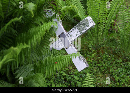 Inclinato, bianco vecchia Croce di legno dietro la felce nel cimitero luterana, Finlandia Foto Stock