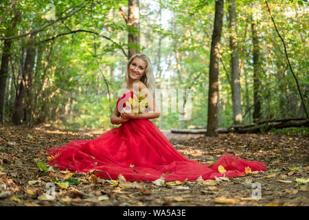 Sorpresa bellissima giovane donna in abito rosso è il puntamento e gridando. Tre quarti di lunghezza studio shot su sfondo grigio. Foto Stock