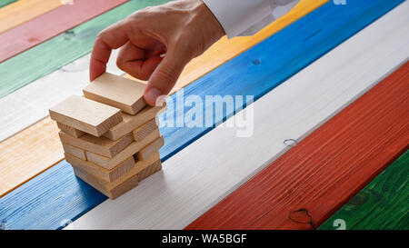 La mano di un uomo d affari con la costruzione di una pila di picchetti di legno su sfondo colorato in una immagine concettuale. Foto Stock