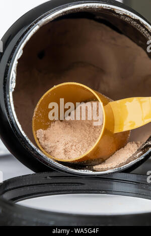 Cucchiaino dosatore in plastica e heap di marrone cioccolato proteine in polvere. Sport Nutrition concetto. Foto Stock