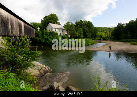 Con un ponte coperto di fronte a lui, un pescatore a mosca getta la sua linea su Mad River in Waitsfield, Vermont. Foto Stock