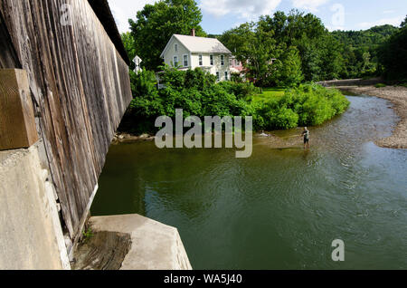 Con un ponte coperto di fronte a lui, un pescatore a mosca getta la sua linea su Mad River in Waitsfield, Vermont. Foto Stock