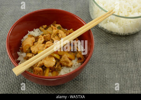 Recipiente rosso di di pollo teriyaki sul riso in bianco con le bacchette di legno e calda tazza di riso cotto Foto Stock