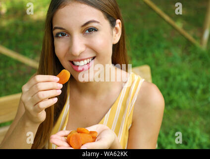 Giovane donna di mangiare la frutta secca nel parco. Cibo sano concetto. Foto Stock