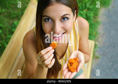 Vicino la vista da sopra di una donna di mangiare le albicocche secche nel parco. Cibo sano concetto. Foto Stock