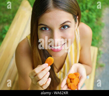 Giovane donna di mangiare le albicocche secche nel parco. Cibo sano concetto. Foto Stock