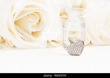 Il giorno di San Valentino regalo con bouquet di rose bianche, fragranza e cuore pendente con diamanti. Copia dello spazio. Soft focus. Regalo di nozze Foto Stock