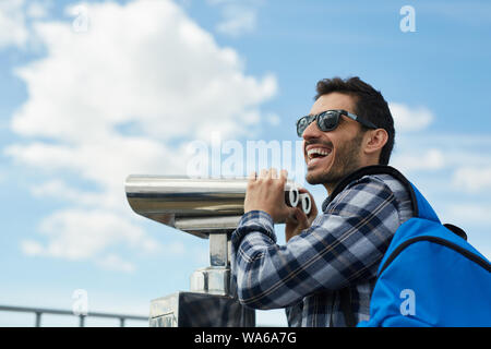 Angolo basso porto caratteristica di entusiasti turista maschio utilizzando un binocolo fisso alla piattaforma di osservazione durante le vacanze, spazio di copia Foto Stock