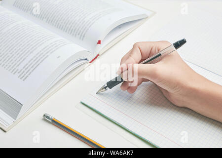 Nella scuola lezione. mano impugna la penna vicino un notebook squadrato. accanto ad esso è un libro e una matita. Sfondo bianco Foto Stock