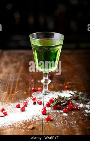 Cocktail verde sulla base di assenzio in un elegante vintage vetro su di un legno marrone. sfondo dello zucchero bianco e mirtilli sono sparsi nei dintorni Foto Stock