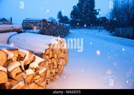 Spalato e legna da ardere in dotazione su una strada di montagna nel paesaggio bavarese durante la nevicata lato illuminato. Foto Stock