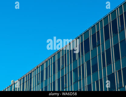 La parte superiore del vetro moderno edificio per uffici in diagonale, cielo blu in background. Foto Stock