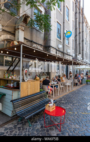 Lisbona, Portogallo - Luglio, 15, 2019: terrazza ristorante, LX Factory street market sotto il ponte di sospensione Ponte 25 de Abril. Foto Stock