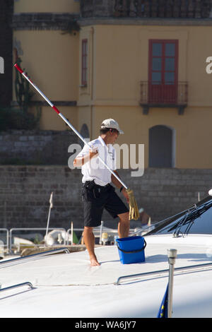 Uomo che usa un lungo mop maneggiato per pulire il ponte di una barca ormeggiata in un porto turistico di Sorrento, Costiera Amalfitana, Italia, Europa Foto Stock