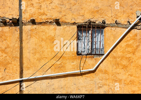 Finestra di vintage con letti in ferro battuto con griglia e un pvc tubo di acqua sul vecchio weathered facciata di una casa Foto Stock