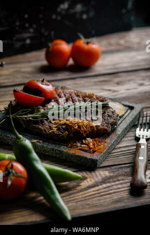 Bistecca alla griglia con coltello e forchetta scolpita sulla pietra nera di ardesia. Bistecca su una calda pietra di marmo. Spazio di copia, sfondo scuro, cibo foto di moda. Foto Stock