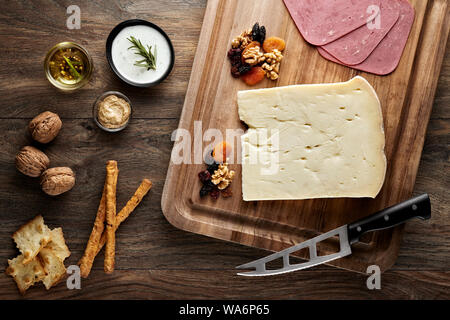 Il formaggio stagionato sul tavolo di legno con tagliere di legno, coltello e puntelli. Vista aerea. Foto Stock