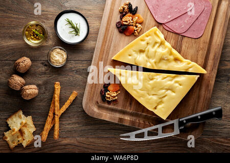 Formaggio gruviera sul tavolo di legno con tagliere di legno, coltello e puntelli. Vista aerea. Foto Stock