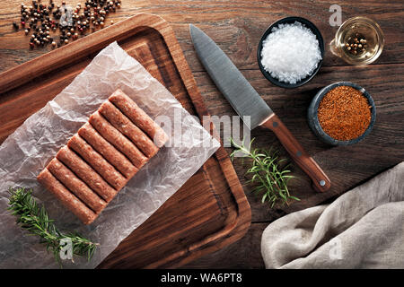 Materie turco polpette inegol sul bianco di carta di cottura e tavolo in legno. Decorate con sale e pepe, carne coltello e igienico. Vista aerea. Foto Stock