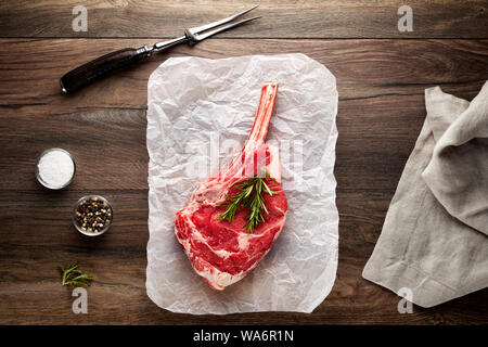 Materie bovine nervatura chop su bianco di carta di cottura e tavolo in legno. Decorate con sale e pepe, carne forcella e igienico. Vista aerea. Foto Stock