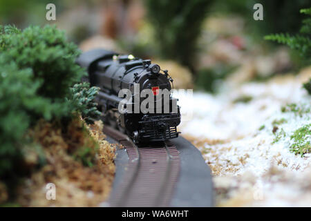 Giocattolo nero treno arrivando dietro l'angolo su un tavolo decorato con verde e sabbia Foto Stock
