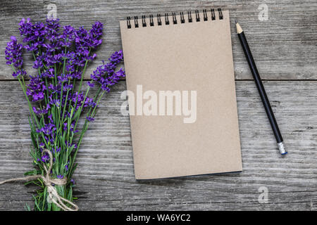 Fiori di lavanda con vuoto notebook carta e matita su legno rustico sfondo. piatto. laici mock up. sfondo festosa. vista superiore Foto Stock