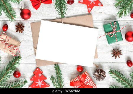 Auguri di Natale carta in cornice fatta di rami di abete, decorazioni, bacche, confezioni regalo e pigne bianco sul tavolo di legno ricoperta di neve. Cristo Foto Stock