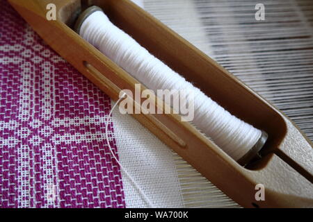 Navetta di tessitura da vicino con la massa bianca e in estate e inverno disegno di tessitura in corso con trama viola Foto Stock