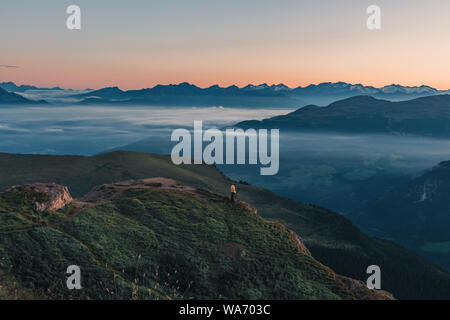 Fotografo di natura in azione. Uomo in piedi sulla montagna sopra una nebbiosa nuvole in attesa di sunrise. mattina paesaggio di montagna Foto Stock