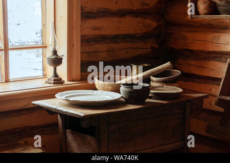 Frammento della parte interna di un vecchio contadino log cabin - una tabella con pavimenti in legno e piatti in ceramica, una lampada di kerosene Foto Stock