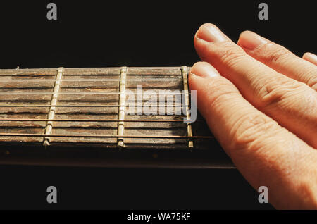 Dita di smorzamento del suono delle corde di una vecchia chitarra acustica, isolata su uno sfondo nero. Collo di una vecchia chitarra acustica con tasti e rus Foto Stock