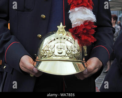 Mons, Belgio. 16 Giugno, 2019. Partecipante di Ducasse processione tiene nelle sue mani casco tradizionale di vigili del fuoco decorate con il rosso e bianco piume Foto Stock