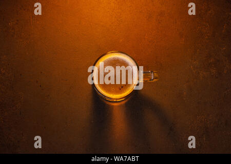 Boccale di birra sul marrone tabella strutturata, il raggio di luce attraverso la birra, vista dall'alto composizione minimalista Foto Stock