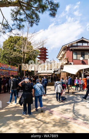 Giappone, Miyajima. Vista lungo la strada principale per lo shopping con bancarelle e negozi su entrambi i lati, affollata di turisti. Red cinque piani pagoda in background. Foto Stock