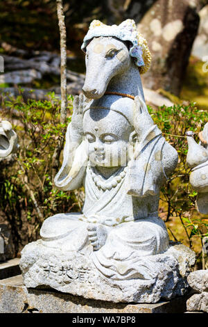 Giappone, Miyajima. Daisho-nel tempio. Piccola pietra Jizo statua di una seduta monaco buddista con entrambe le mani tenendo un testa di cavallo hat. Foto Stock